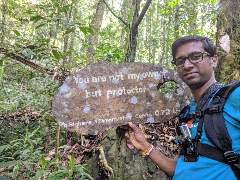 Caption: A photo of Ilankovan holding a rusty sign in a forest that says, “You are not my owner but protector.” (Courtesy of Local Guide @IlankovanT)