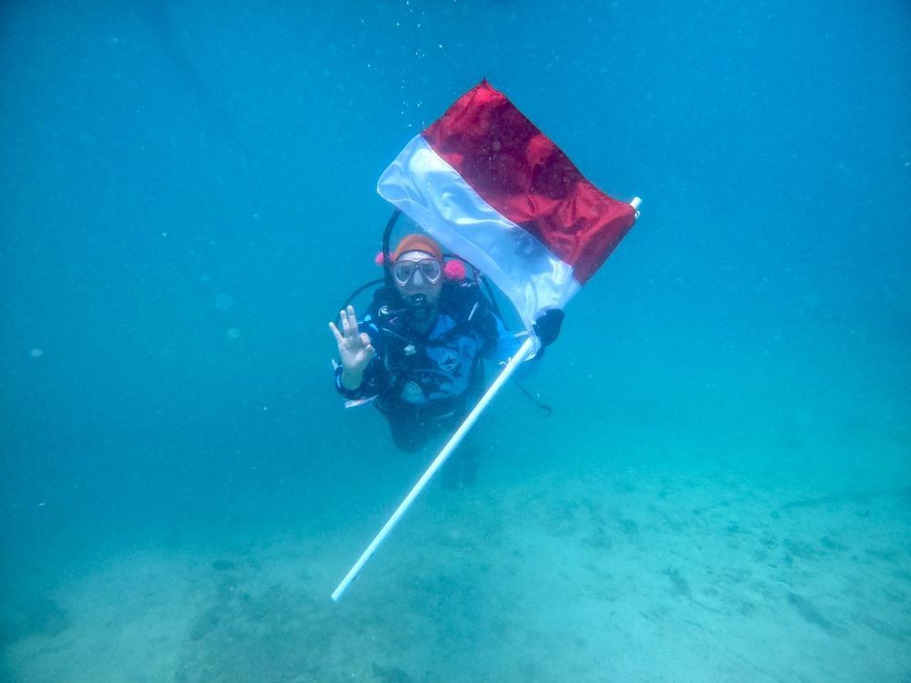 Caption: An underwater photo of Local Guide @indahnuria holding the Indonesian flag. (Local Guide @indahnuria)