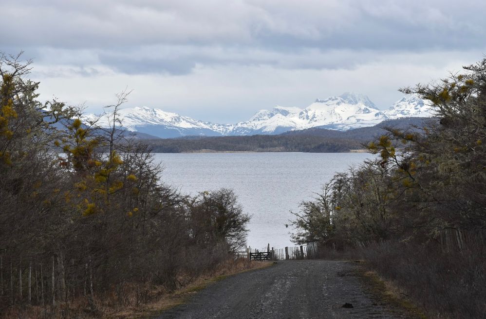 Caption: A photo of a dirt road leading down to Lake Yehuin in Argentina, with snow-covered mountains in the distance. (Local Guide @FaridMonti)