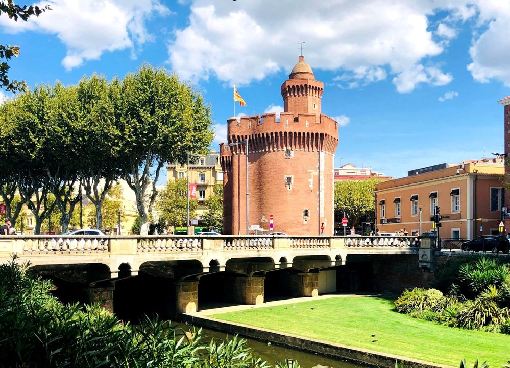 Légende: Une photo du musée Le Castillet à Perpignan, France, avec le drapeau catalan flottant au-dessus et un canal passant sous le pont en face. (Local Guide @BorrisS)
