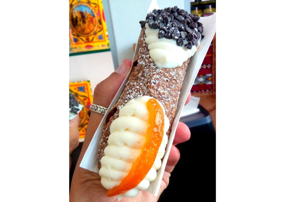 Caption: A photo of a hand holding a large cannolo with different toppings on both ends. (Local Guide @BorrisS)