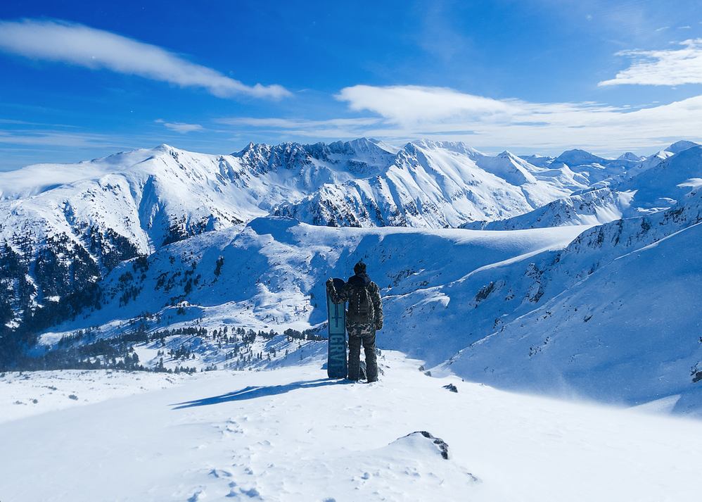 Caption: A photo of a person holding a snowboard and looking at the snowy peaks of Pirin Mountain, Bulgaria. (Local Guide @travelwithcarlo)