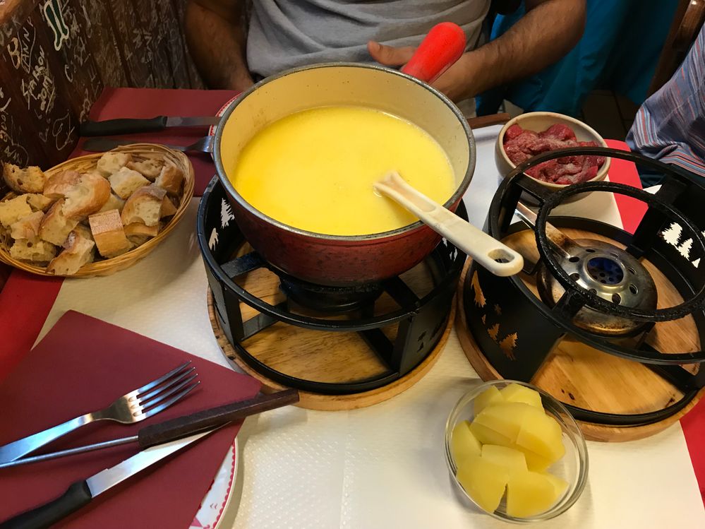 Caption: A photo of a pot of melted cheese, a basket of bread, cut up boiled potatoes and salami in small bowls, and fondue equipment on a table at Le Refuge des Fondus in Paris. (Local Guide @GasparKaren)