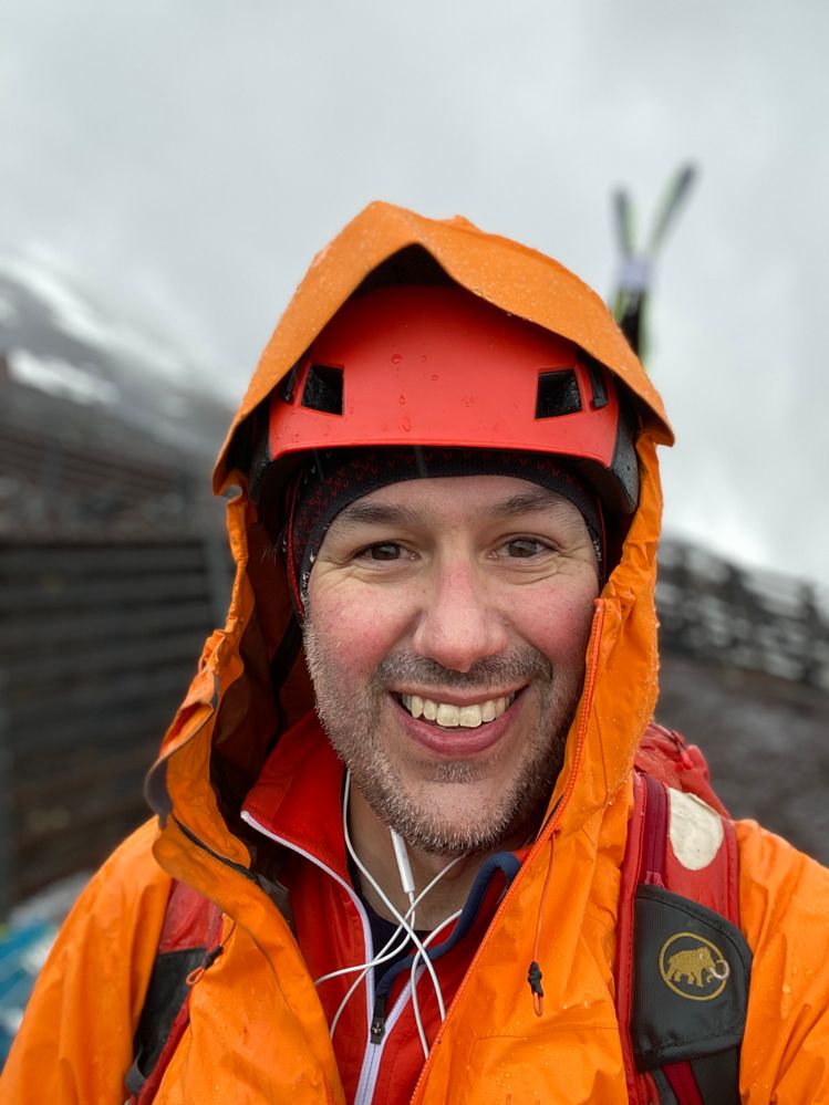 Caption: A photo of Ian smiling in orange apparel during a bike and ski trip on Mount Fuji.
