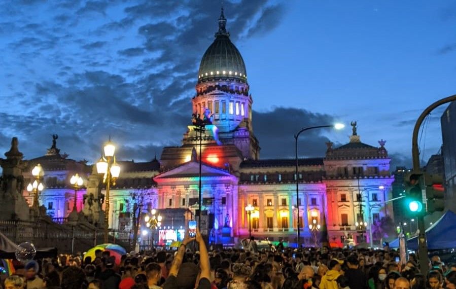 Caption: photo of the Buenos Aires Congress in the evening, painted with lights that represent the colors of the LGBT+ flag.