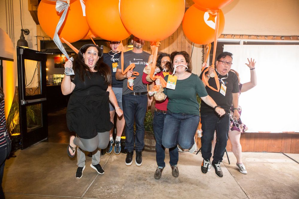 Caption: A photo of Traci (left) jumping with Local Guides at the 2016 summit, with giant orange balloons.