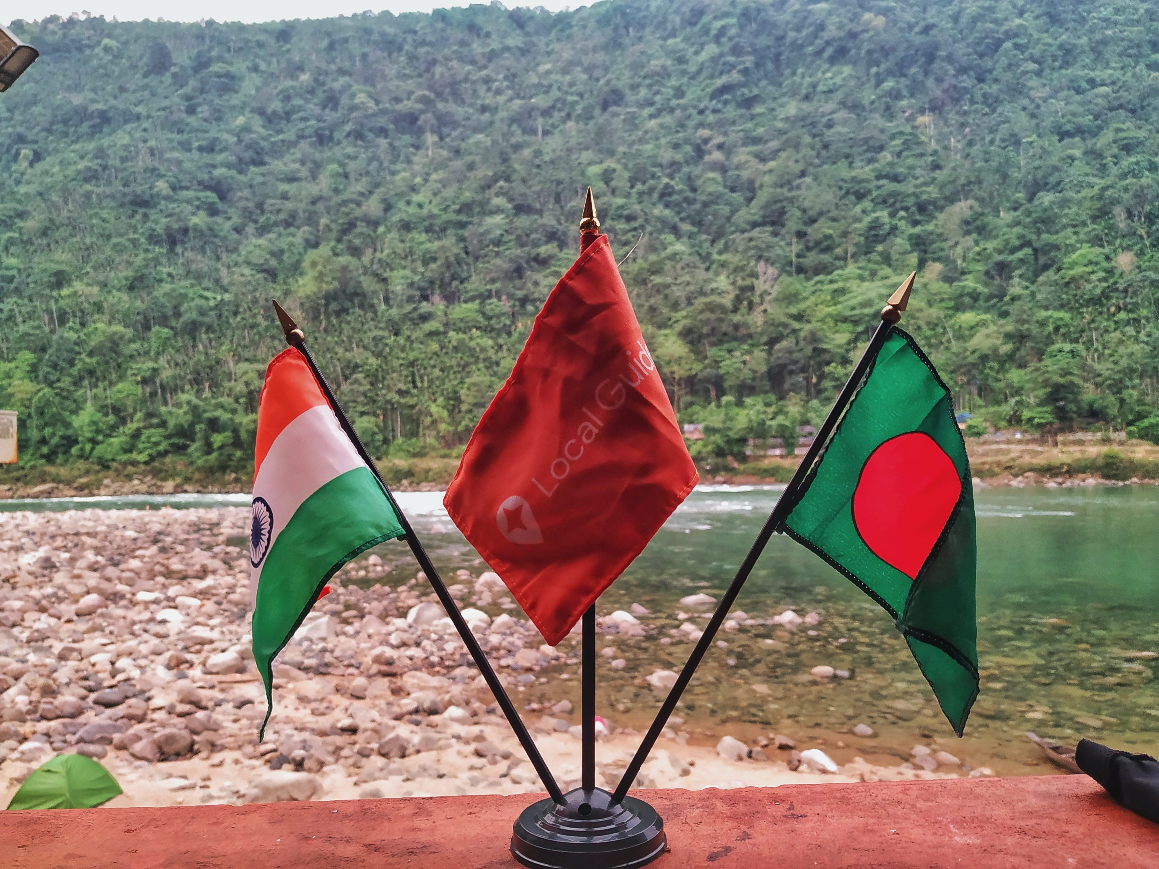 A flag stand there India -local guides and Bangladesh flag  back side stone full river bank and clear water river and green hills