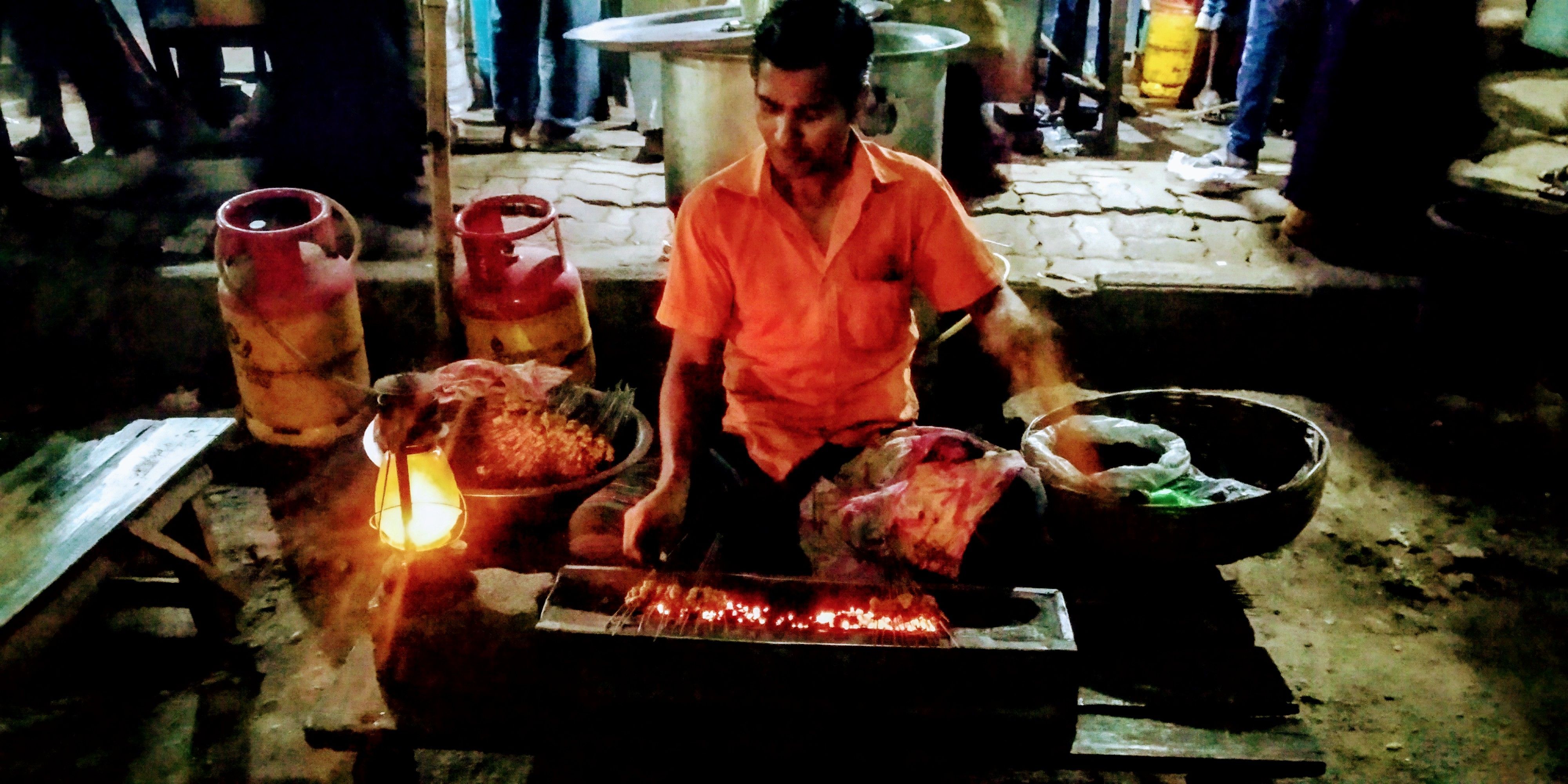 Caption: A hawker making BBQ Kebab seating beside the road.