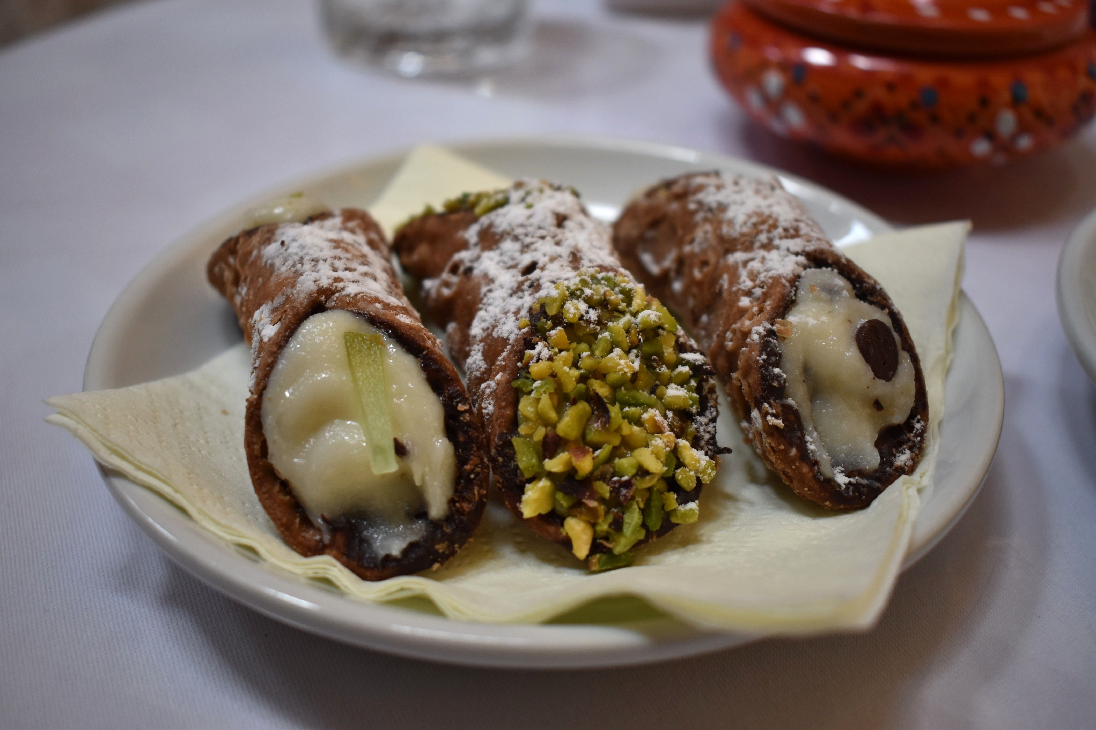 Caption: A photo of three cannoli pastries with ricotta cream, pistachio, and lemon, placed on a napkin in a small plate. (Local Guide @MoniDi)