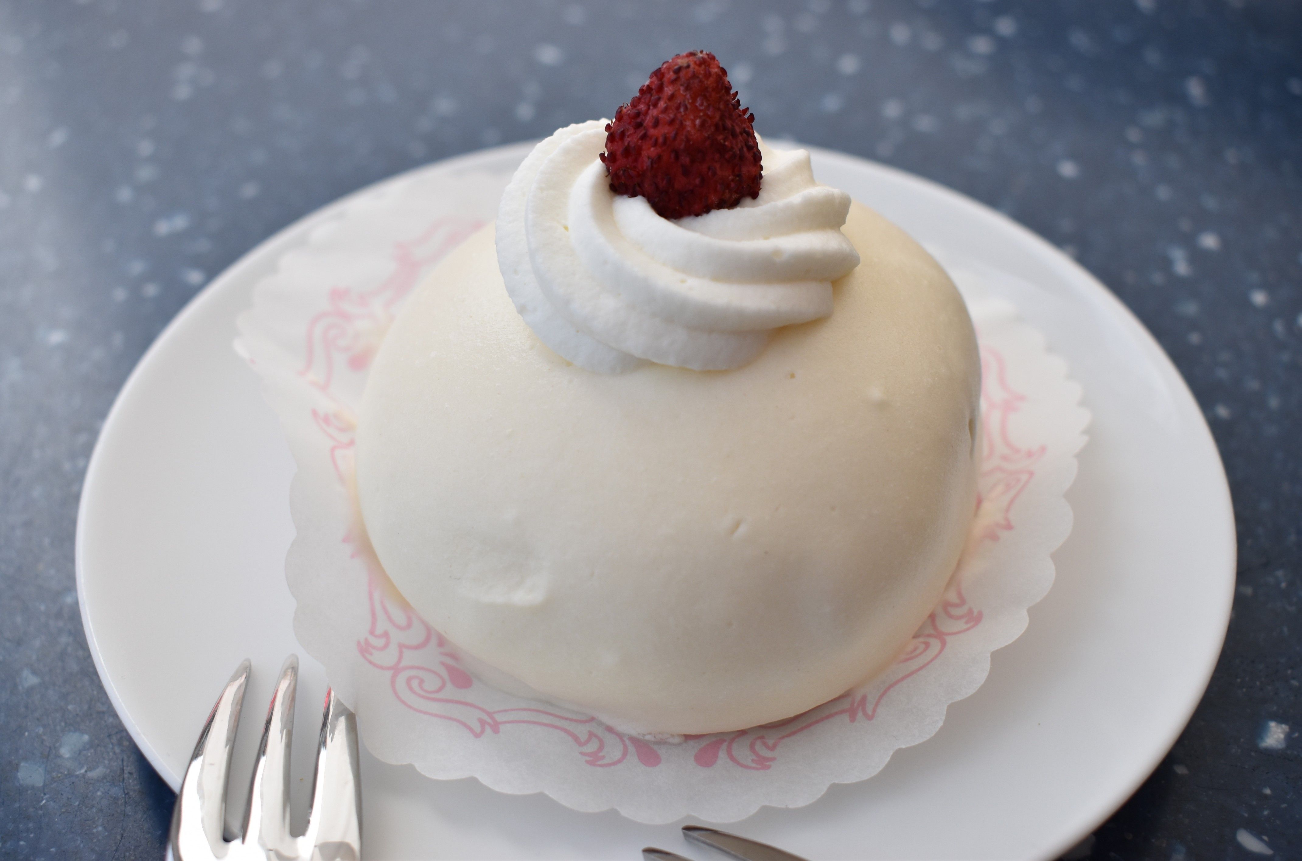 Caption: A photo of a white round Delizia al Limone cake on a white plate, with whipped cream and a wild strawberry on top. (Local Guide @MoniDi)