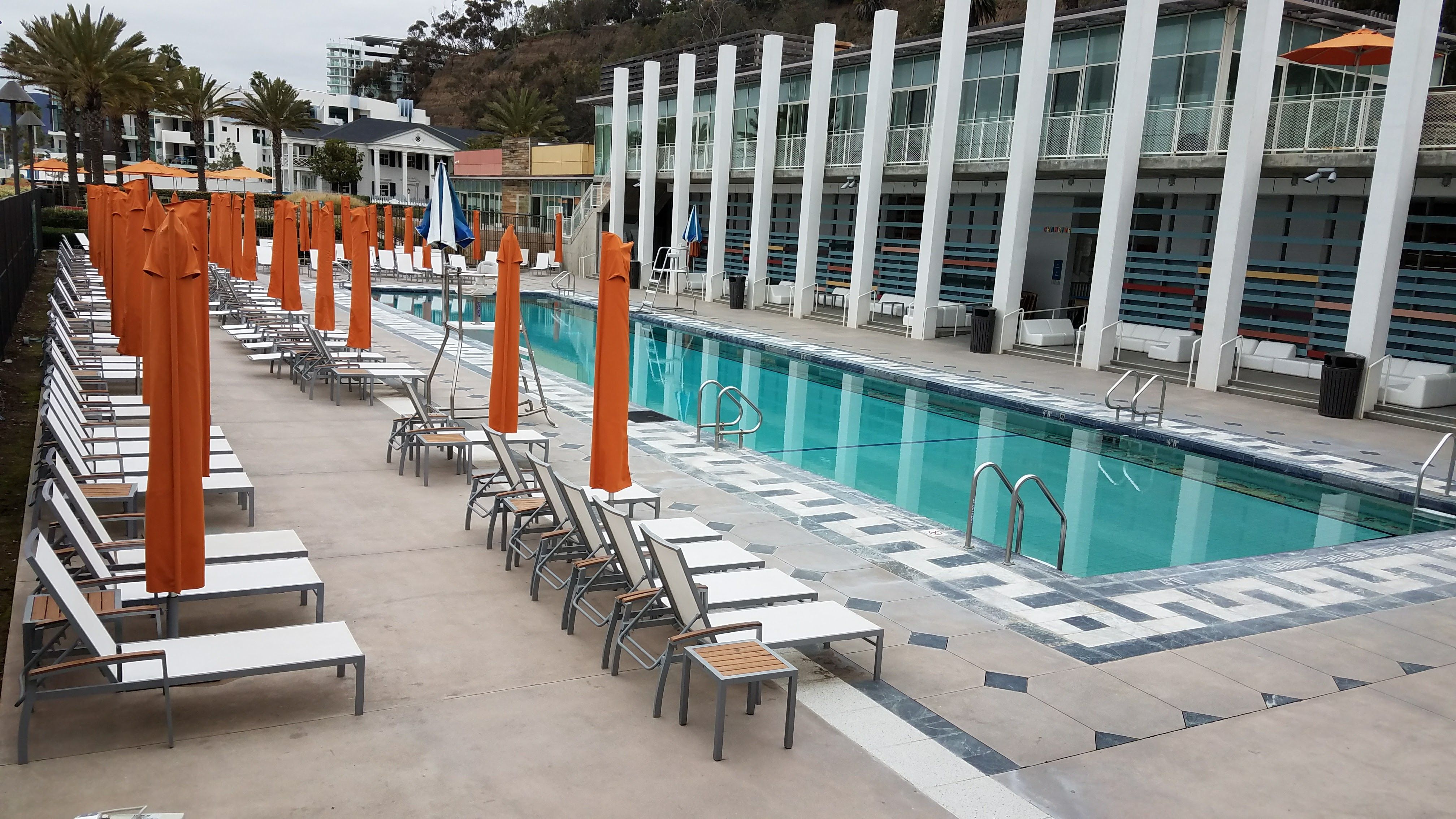 Caption: A photo of a pool surrounded by beach chairs and orange umbrellas at Annenberg Community Beach House in Santa Monica, California. (Local Guide Abbi Coursolle)