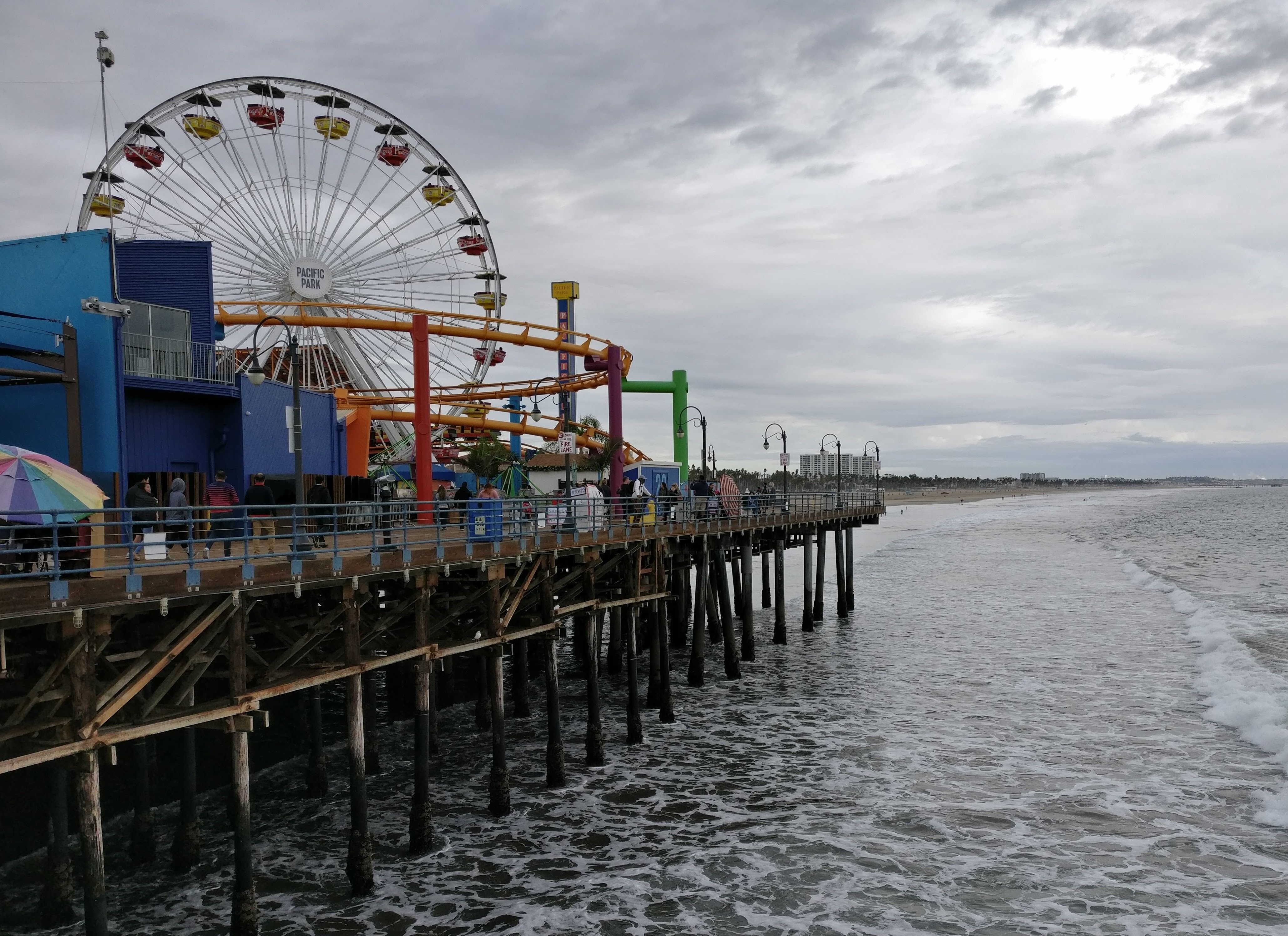 Caption: A photo of a ferris wheel, roller coaster, and other attractions at the pier at Santa Monica Pier Aquarium taken from the water in Santa Monica, California. (Local Guide Rholais Lii)