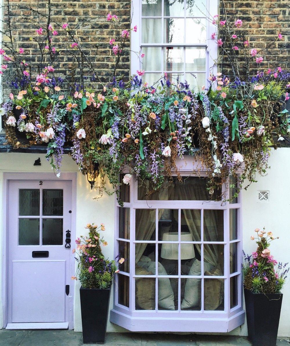 Caption: A photo of a building with a purple door and large purple painted bay window surrounded by different colored flowers. (Courtesy of Bella Foxwell)