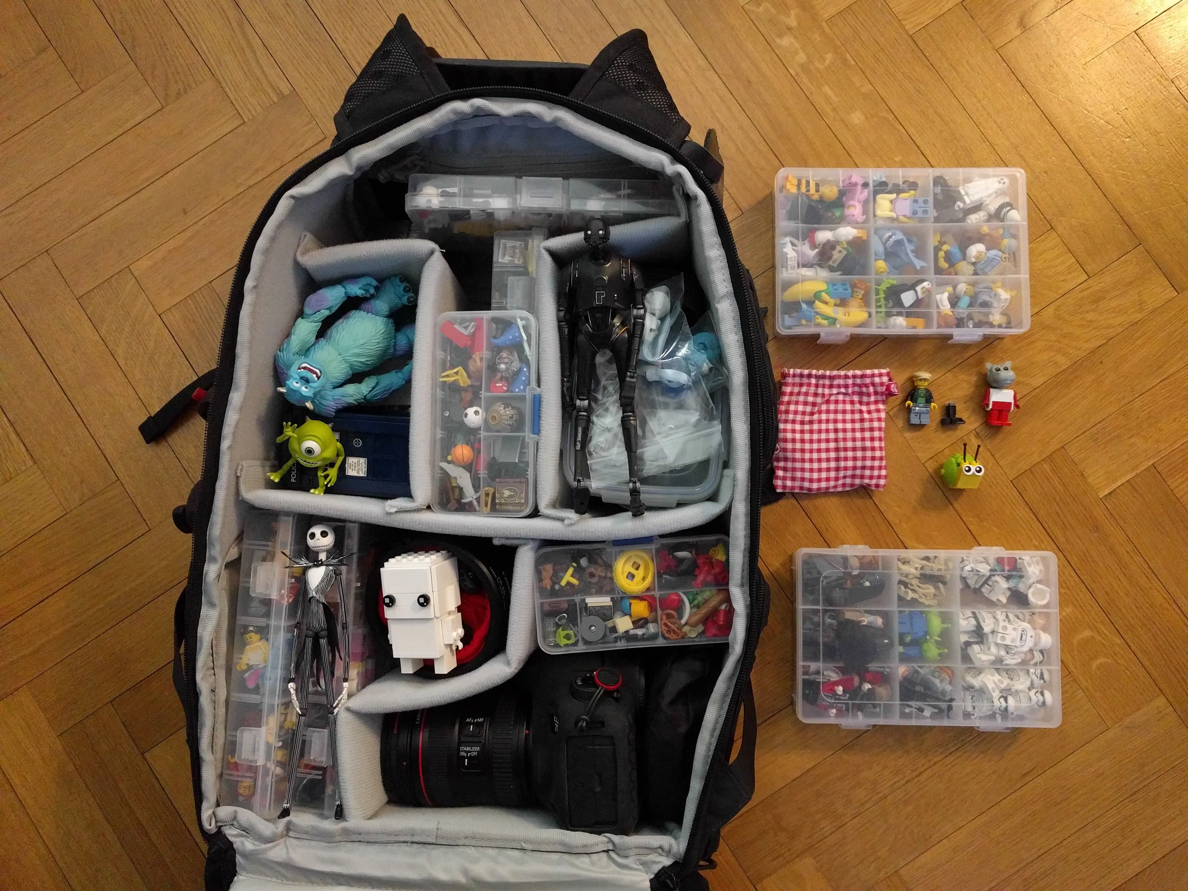 Caption: A photo of an open backpack on the floor filled with clear plastic cases of toys and figures as well as a DSLR camera. Next to the backpack are two clear plastic cases filled with LEGO minifigures. (Courtesy of Julien Ballester)
