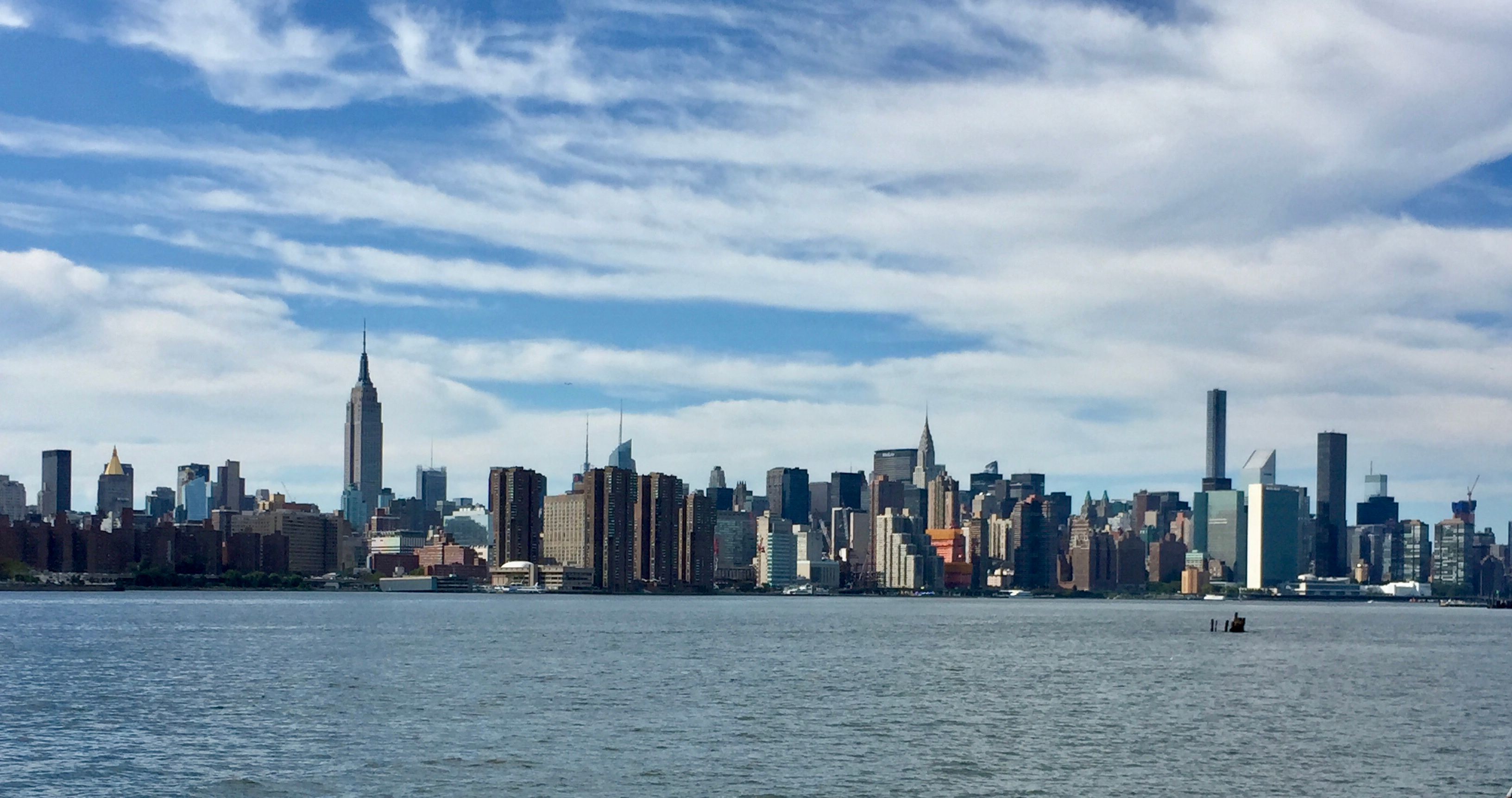 Caption: A photo of the Manhattan skyline taken across the water on a partly cloudy day.