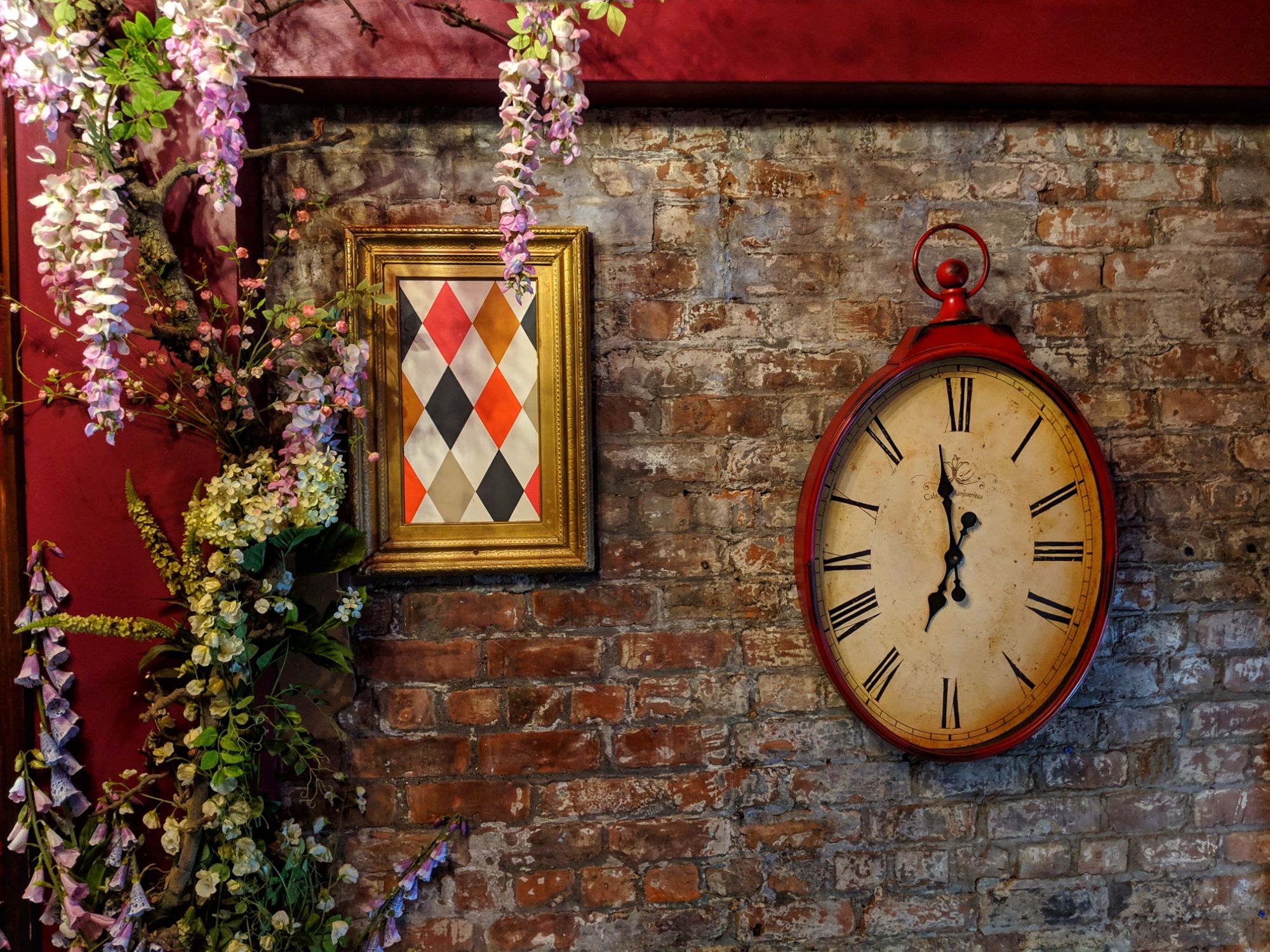The entrance to the Richmond Tea Rooms Manchester. On the  brick wall  is a misshaped clock, a picture of harlequin pattern and some climbing plants.