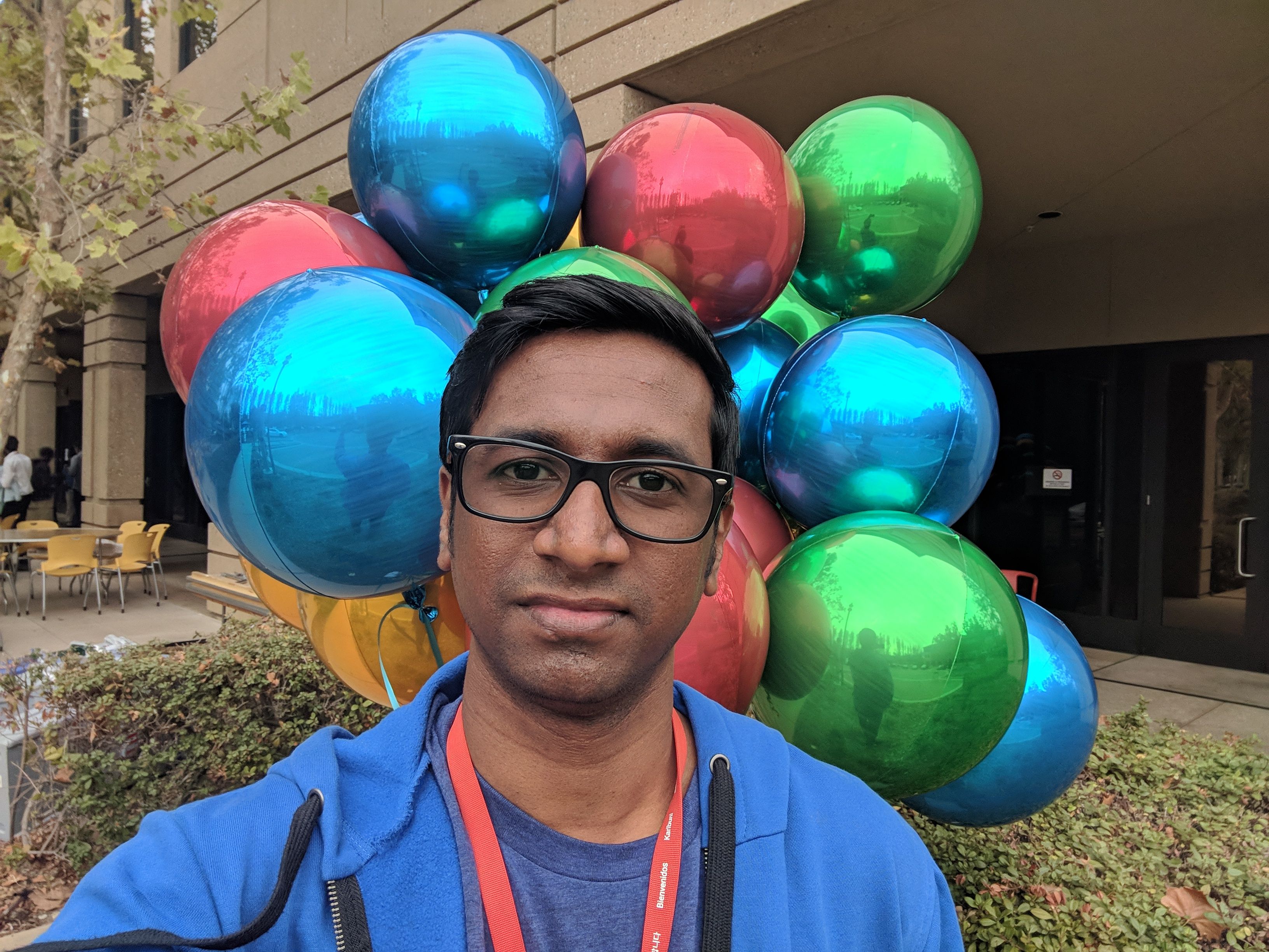 Caption: A photo of Local Guide @IlankovanT standing in front of blue, red, green, and yellow balloons taken outdoors at Connect Live 2018. (Local Guide @IlankovanT)