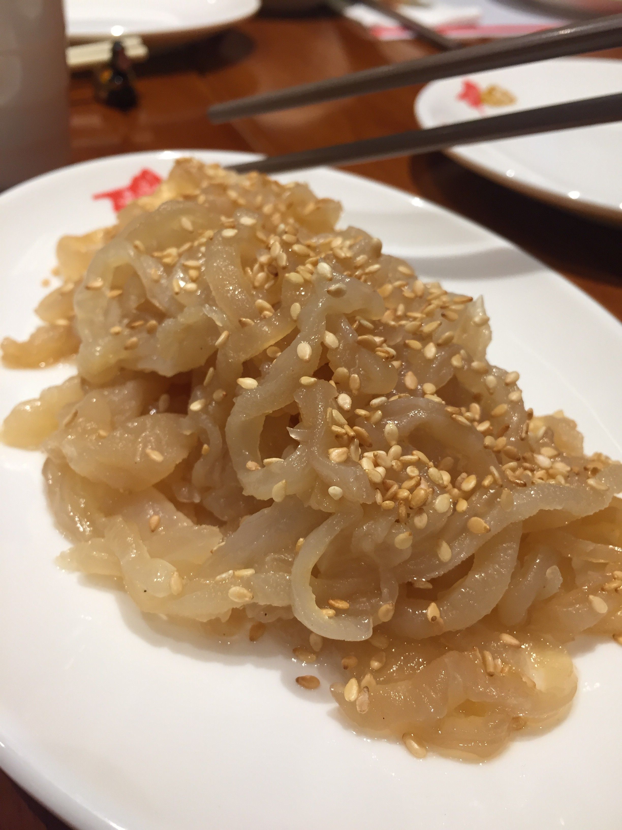 Caption: A photo of the jellyfish appetizer with sesame seeds sprinkled on top on a white plate at Kam’s Roast in Singapore.  (Local Guide @AngieYC)