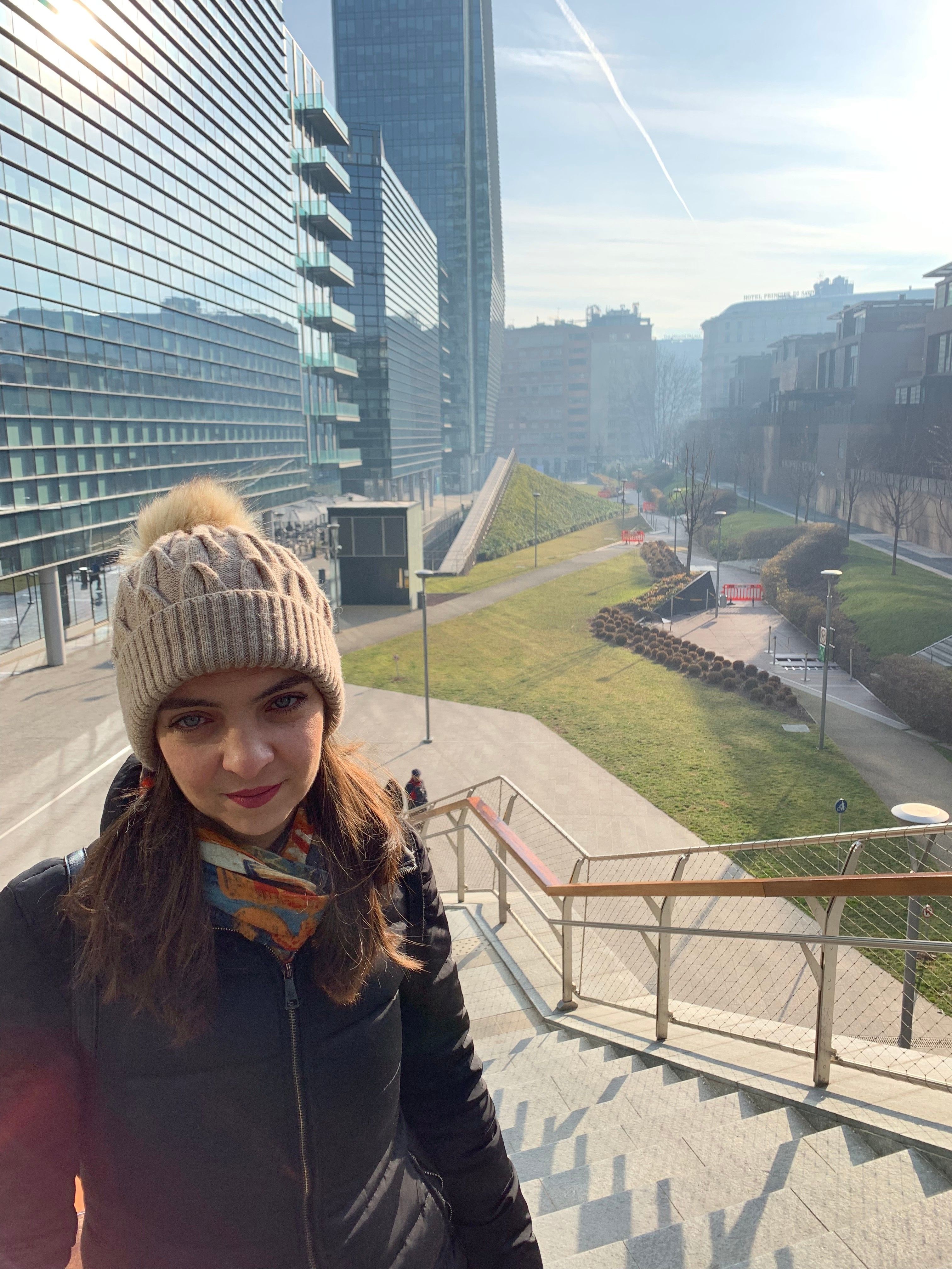 Caption: A photo of me with a business buildings, stairs and a grassy valley behind. Milan, Italy (Local Guide MashaPS)