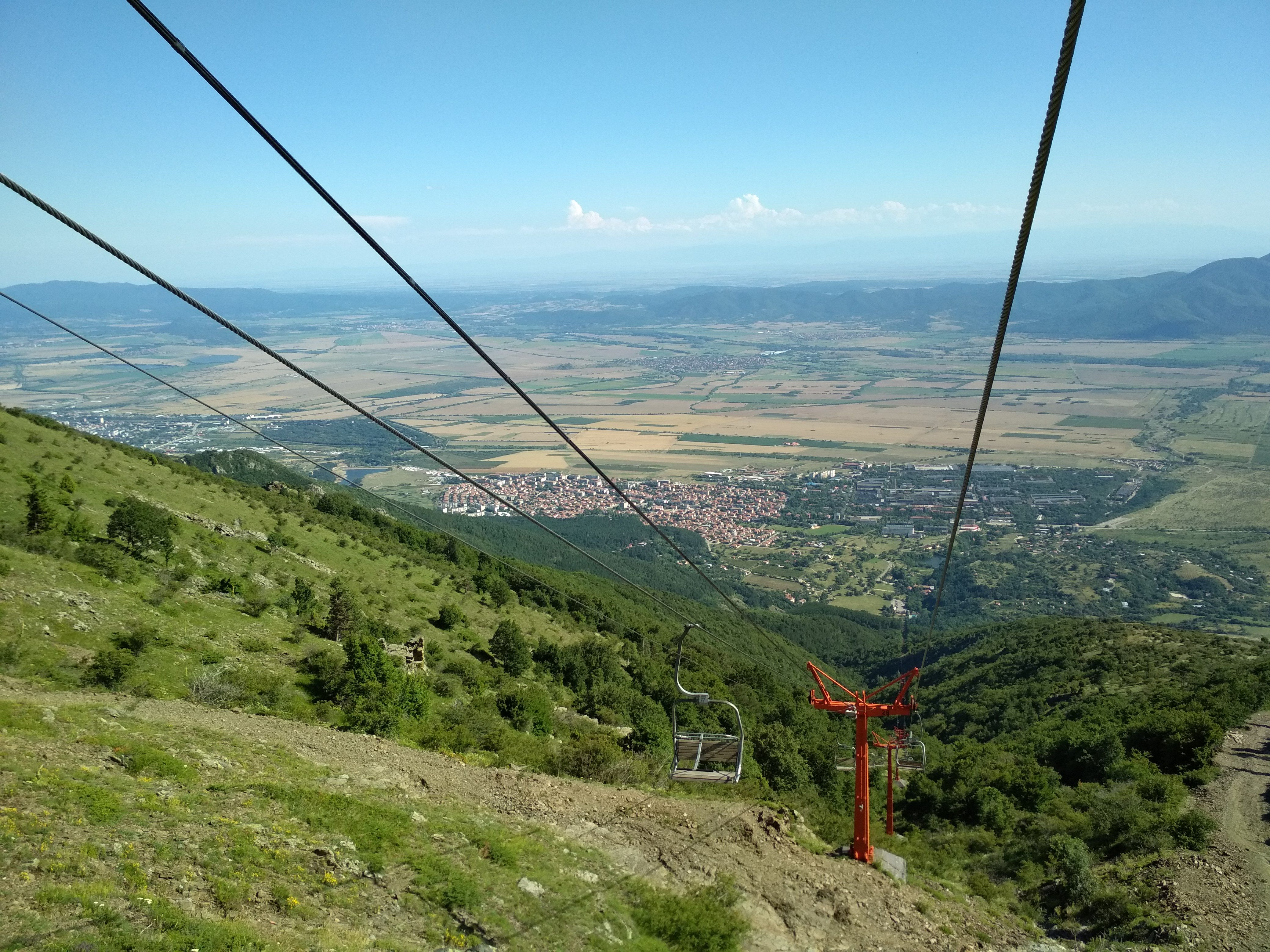 Didascalia: Una foto della città di Sopot, in Bulgaria, vista dalla una funivia, circondata da campi e montagne. (Local Guide @DeniGu)