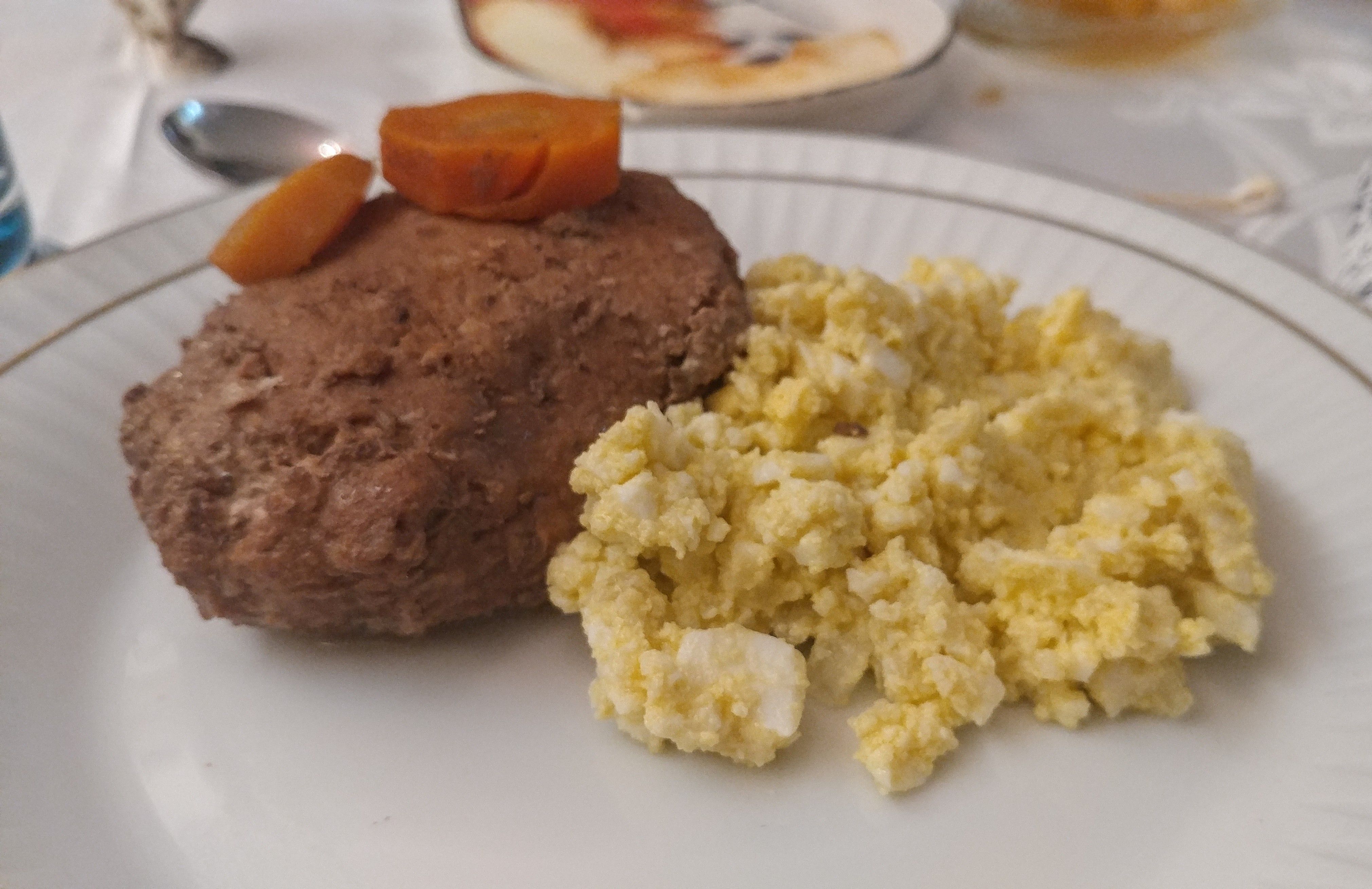 Caption: Gefilte fish with two slices of carrot on the top, served with an egg, potato and onion salad.
