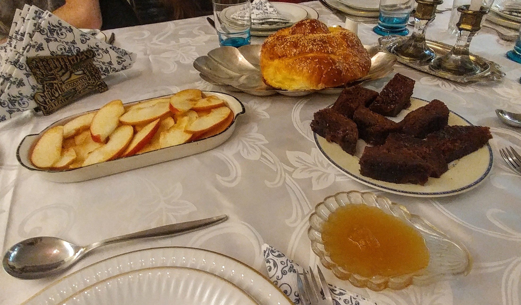 Caption: Dishes with sliced apples, honey, a round challah and slices of lekach