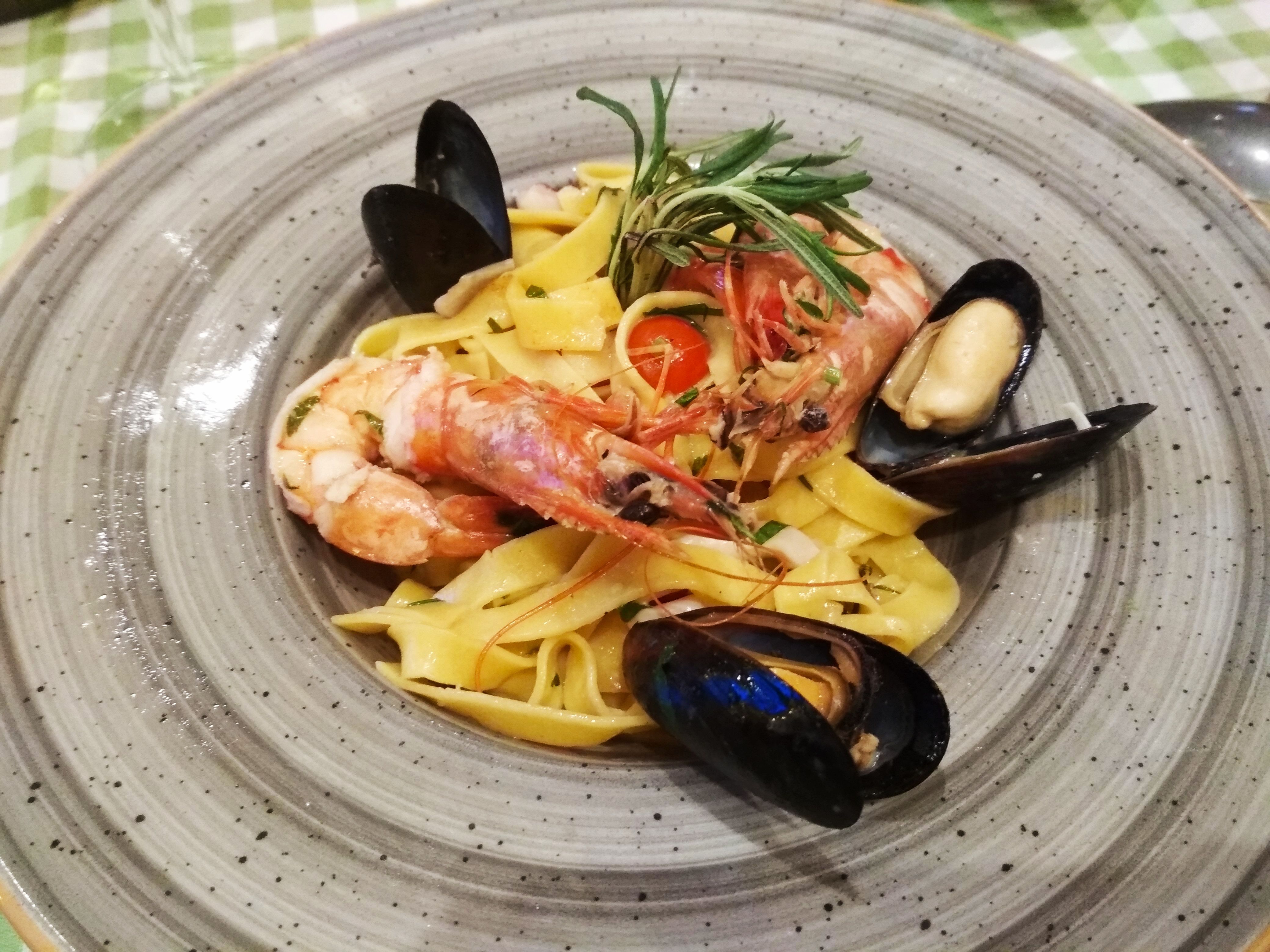 Caption: A photo of a grey plate with tagliatelle pasta, topped with prawns, mussels, with a cherry tomato at The Old House-Iztok in Sofia, Bulgaria. (Local Guide @DeniGu)