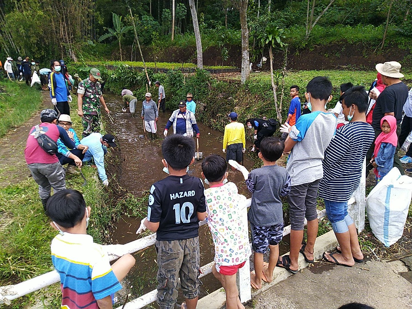 Caption: A photo of kids lined around a barrier watching adults clean garbage out of a river.  (Local Guide @br14n)