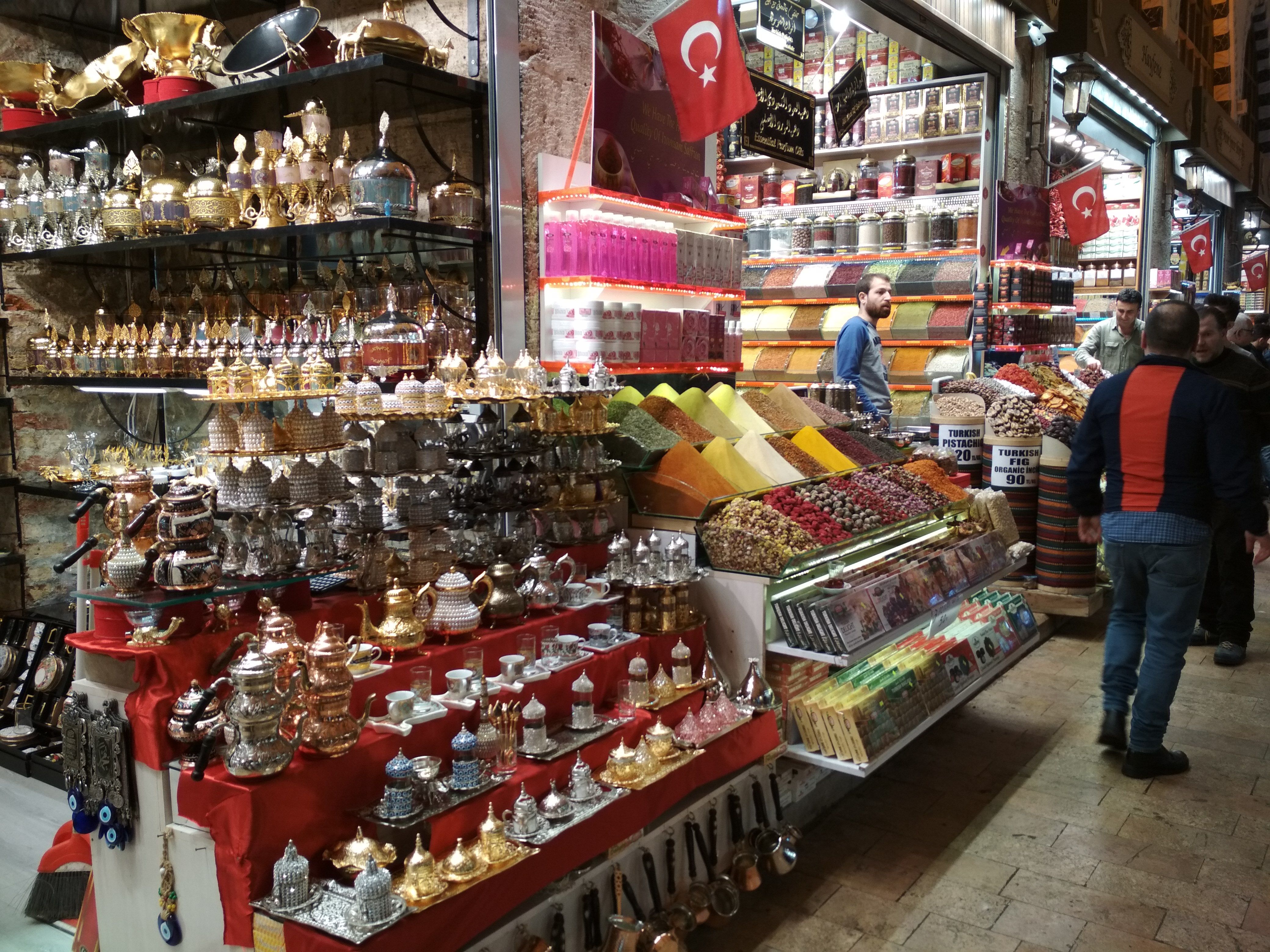 Caption: A photo of two shops inside the Egyptian bazaar in Istanbul, Turkey. The left shop has a variety of metal coffee pots and cups on display, while the shop on the right sells different spices in various colours. (Local Guide @DeniGu)
