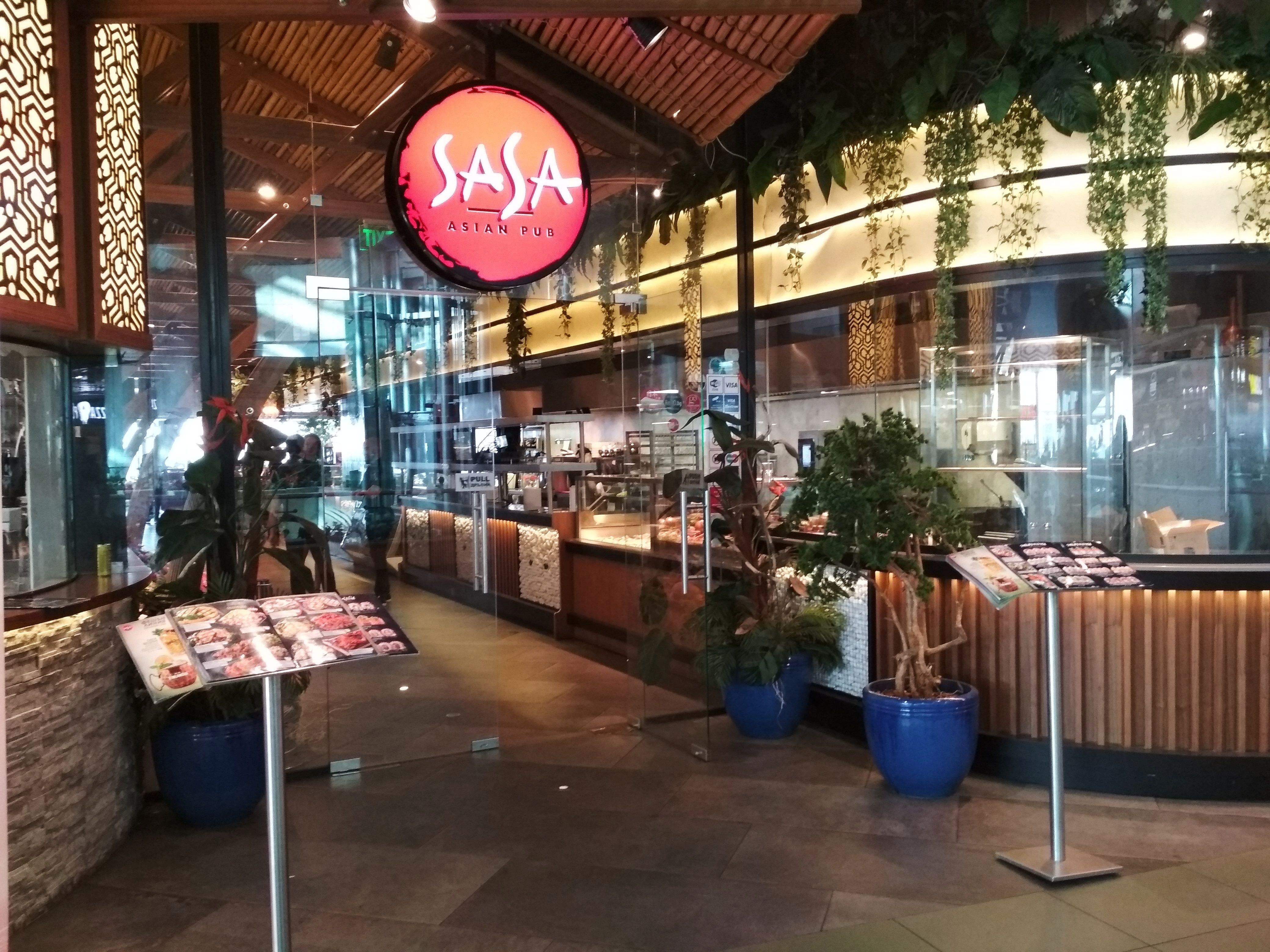 Caption: A photo of the exterior of the SASA restaurant, showing a wheelchair accessible entrance through glass doors, two stands for the menu, and a sign that says “SASA Asian Pub” in Sofia, Bulgaria. (Local Guide @DeniGu)