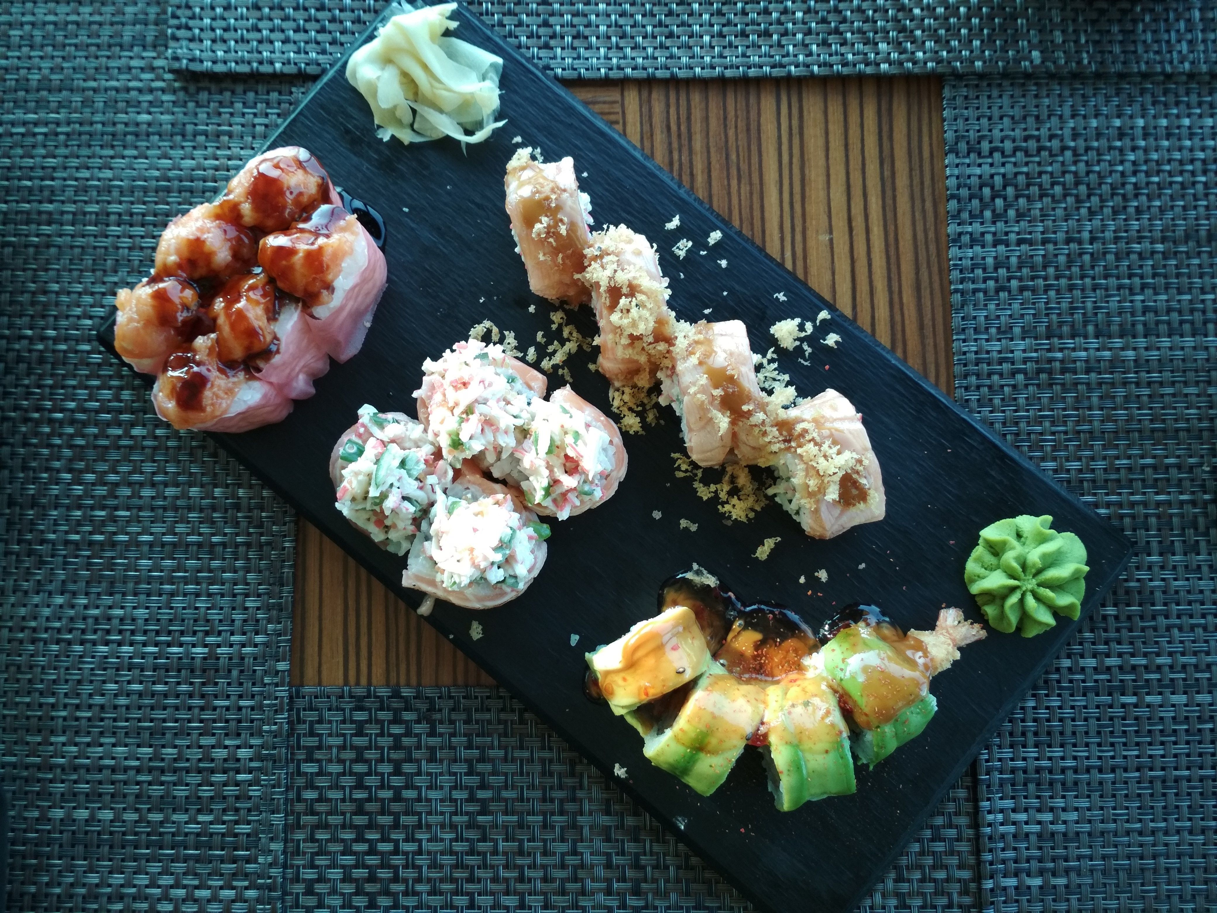 Caption: A photo taken from above that shows a rectangular plate with different kinds of sushi rolls: with salmon paste and sauce, crab meat salad, salmon and panko breadcrumbs, avocado and crispy shrimp. The plate is framed by four placemats and was taken at SASA in Sofia, Bulgaria. (Local Guide @DeniGu)