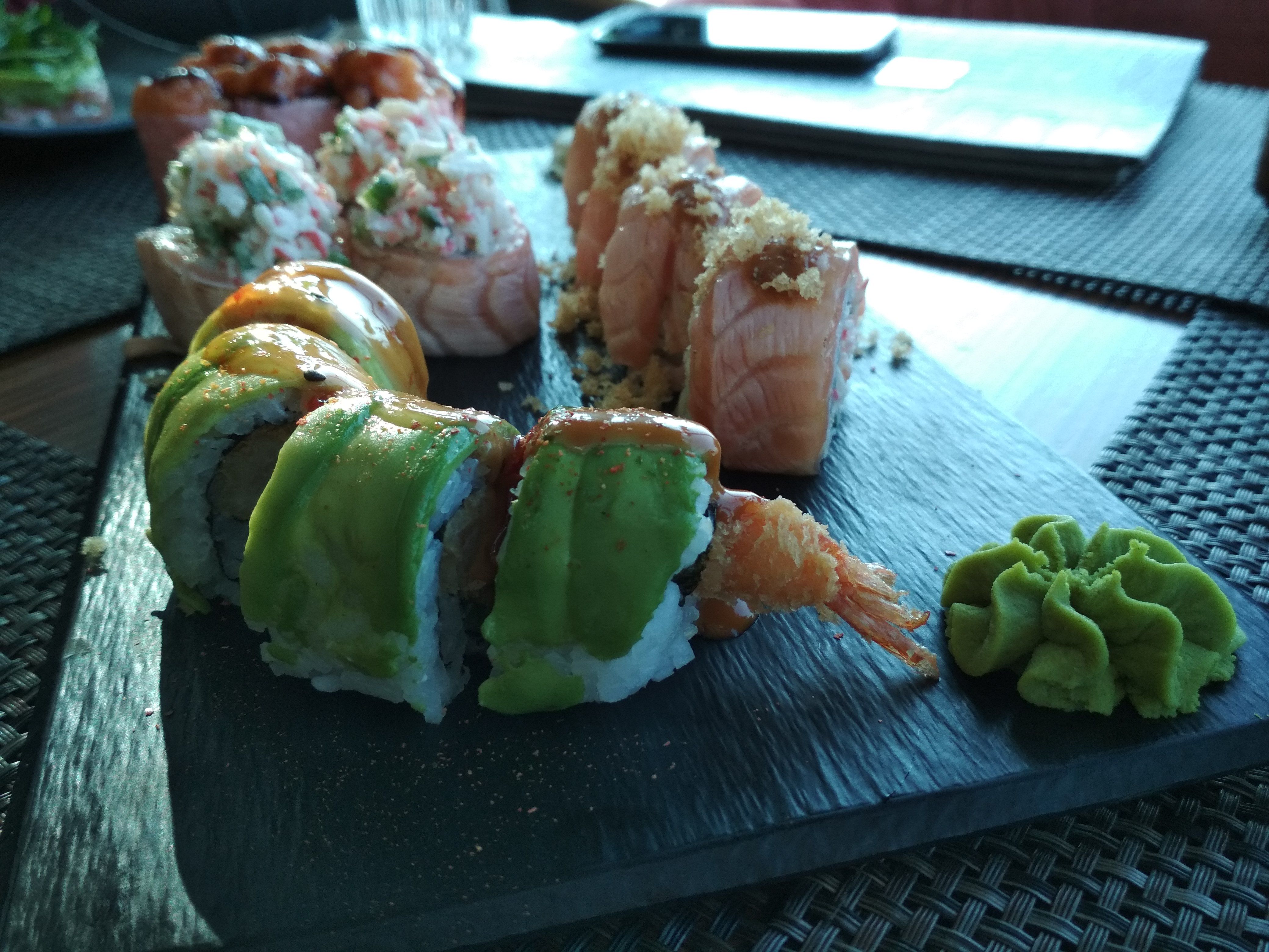 Caption: A close-up photo of a plate with various sushi rolls, focusing on four rolls with avocado and shrimp, with the crispy shrimp tail sticking out of one of them, at SASA, Bulgaria. (Local Guide @DeniGu)