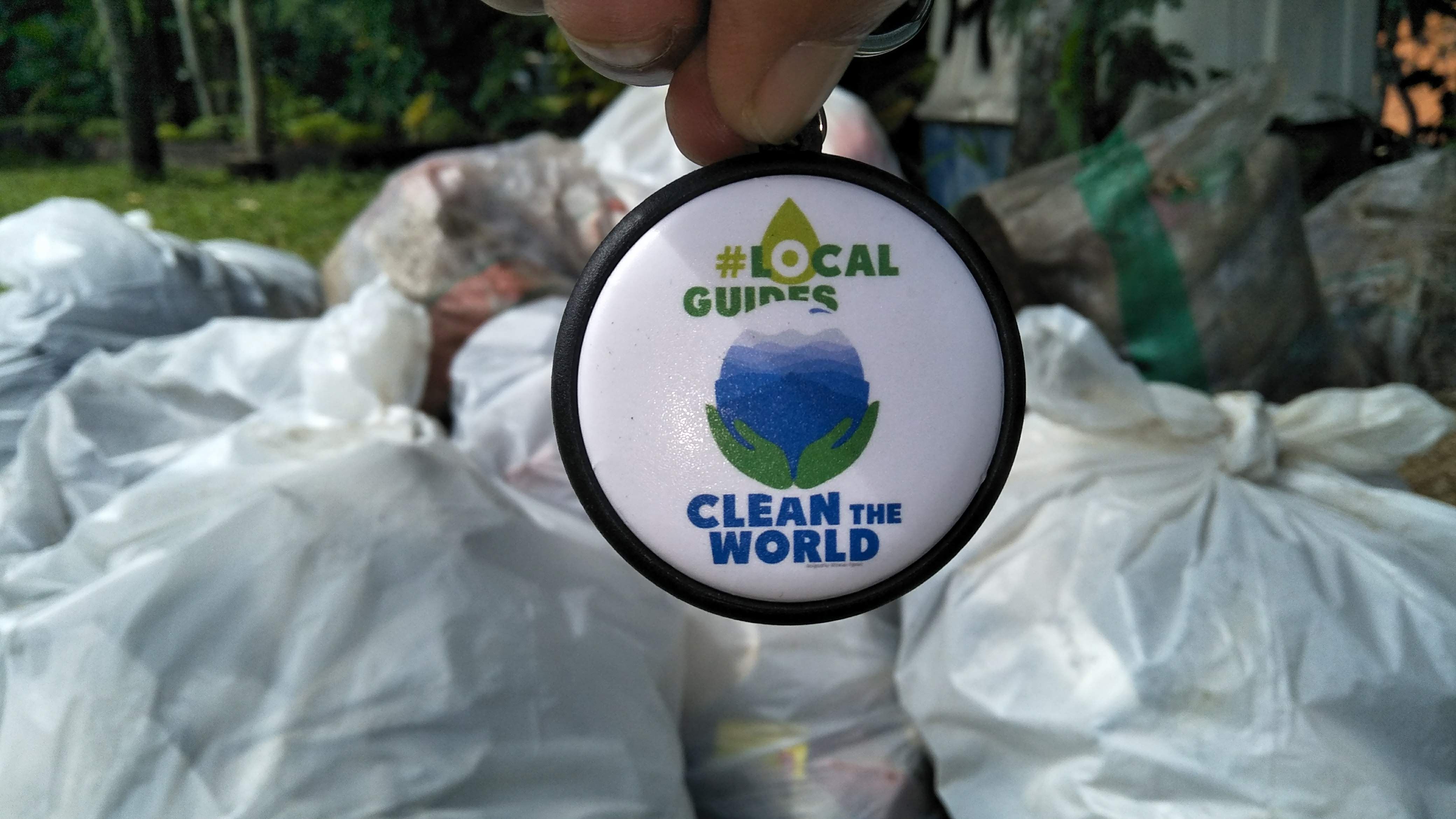 Local Guides Clean The World Pin dengan latar belakang karung sampah