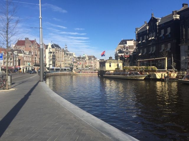 Caption: one of the main streets along of the canals with houses on the sides and a boat with a Netherlands flag.
