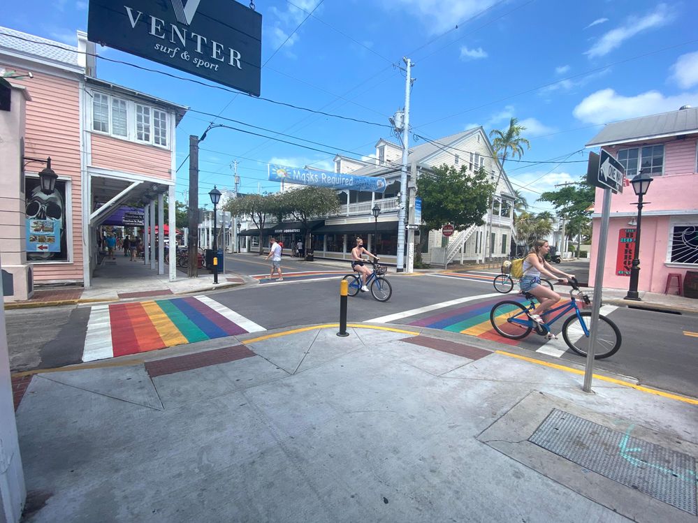 Caption: A photo of the Rainbow Crosswalk (Key West) in Florida, USA, and folks on bicycles riding in the street. (Local Guide Lara Mayberry)