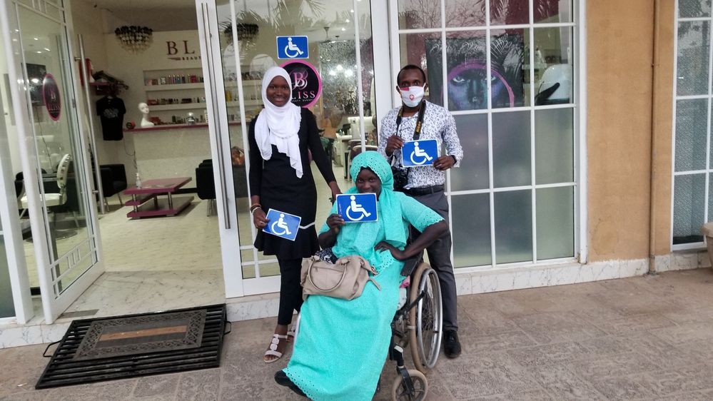 Caption: A photo of Local Guide Maimuna Jabbie (left), Ramatoulie from the Gambia Federation of The Disabled (middle), and Alpha (right) at The Village shopping center in Senegambia, The Gambia, testing the new wheelchair ramps and putting accessibility stickers on the various restaurants. (Courtesy of Local Guide @Alffiiy)