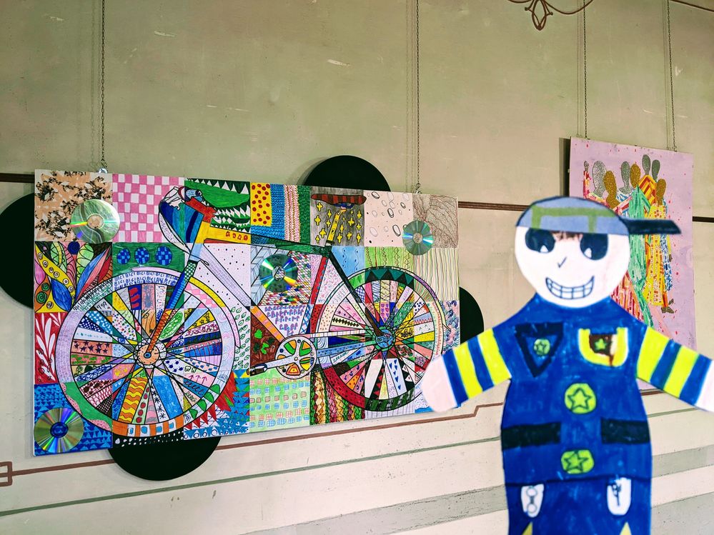 Caption: Flat Stanley with on the background a paint made by children of a school exhibited at the Biennale of Children's Art