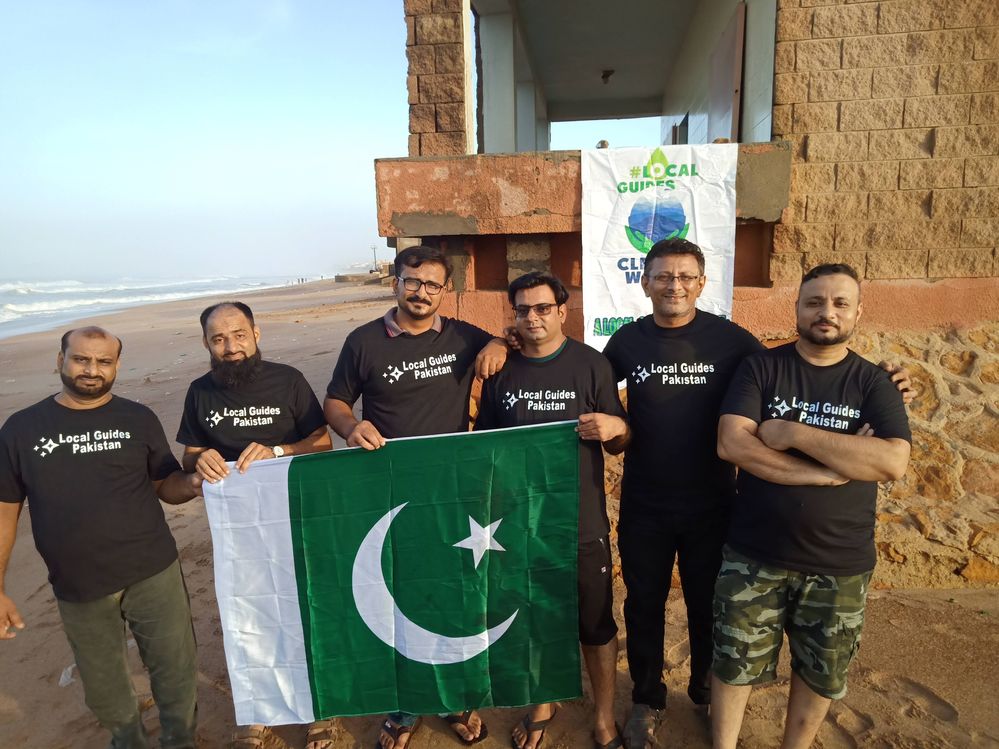 Caption: A photo of Kashif and fellow Local Guides from Pakistan holding the national flag on a beach, with a “Local Guides Clean the World” banner behind them. (Courtesy of Local Guide @KashifMisidia)
