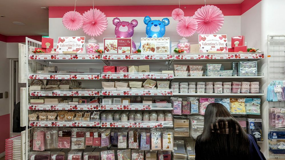 Caption: A photo of a student browsing shelves of packaging supplies in various patterns, with paper flowers, bear balloons, and “Valentine’s Day” signs arranged at the top. (Courtesy of Local Guide @Izumi)