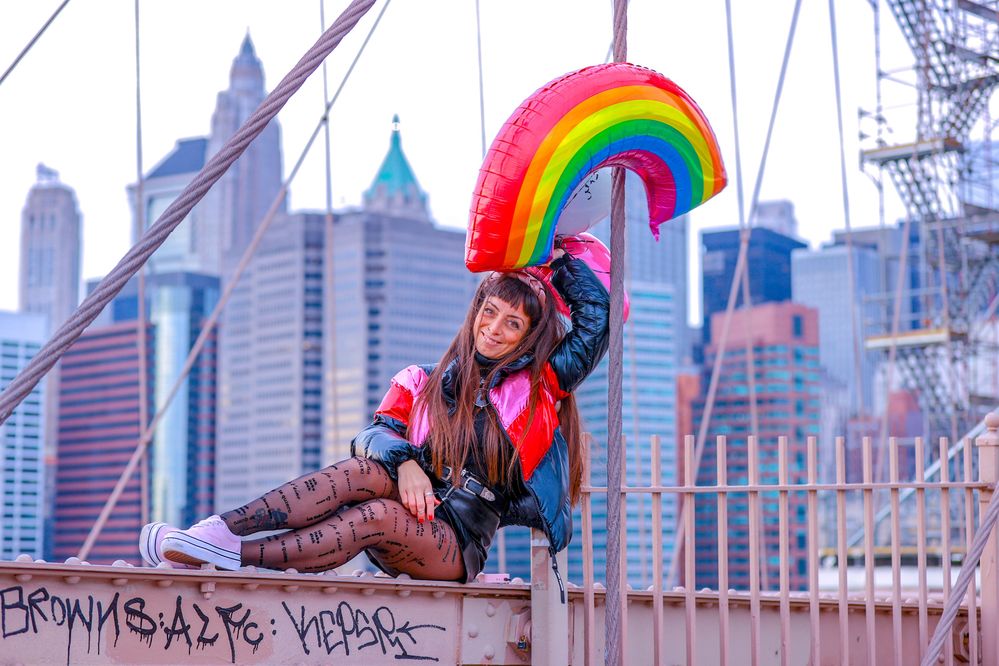 Caption: A photo of Local Guide Kiara Di Paola sitting on the Brooklyn Bridge in New York City and holding a rainbow balloon. (Courtesy of Local Guide @Kiariladyboss)