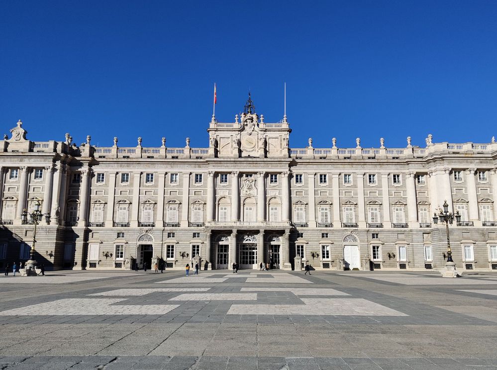 Caption: A photo of the white facade of the Royal Palace of Madrid set against a bright blue sky.