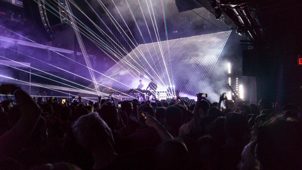 Caption: A packed crowd watches an electronic music concert with laser lights and smoke machines at concert venue Terminal 5 in New York City by Dimitrios Spyropoulos