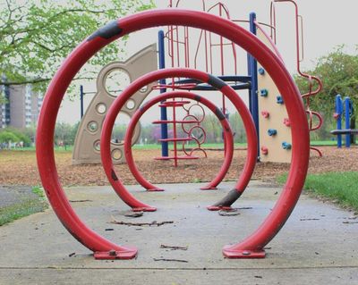 Three large, red, circular metal sculptures in a playground framing a jungle gym behind it (Getty Images)