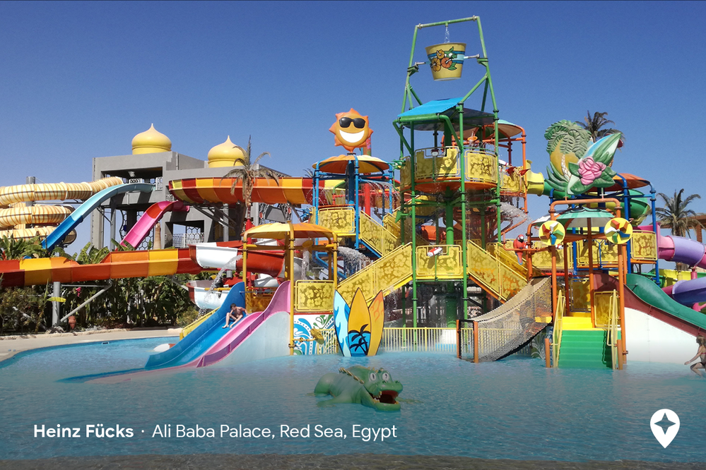 Caption: A photo by Heinz Fücks of a colorful children’s waterpark in Egypt featuring slides, stairs, and ramps leading to a large, shallow paddling pool