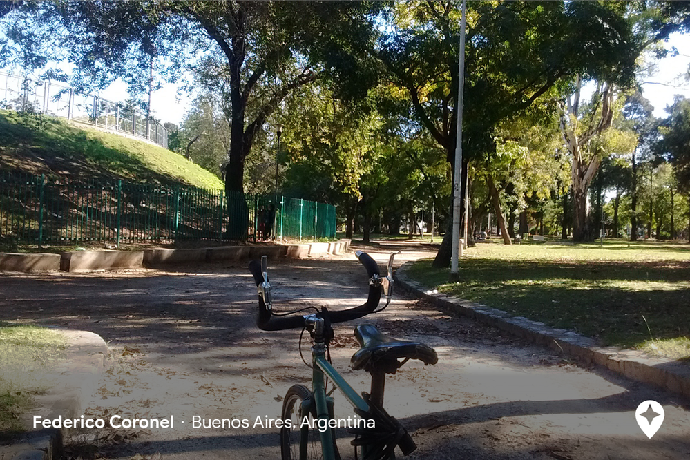 Caption: A photo of a bike on a concrete path in a park in Buenos Aires with large trees and grassy areas (Federico Coronel)