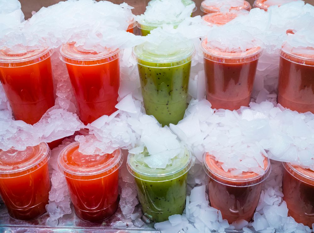 Caption: A photo of orange, green, and red fruit smoothies in plastic cups sitting on ice. (Getty Images)