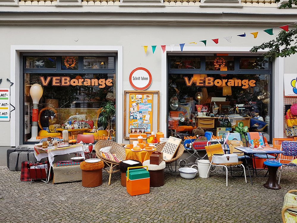 Caption: A photo of the exterior of thrift store, VEB Orange, in Berlin, with furniture and home goods in front of the window displays. (Local Guide Max Mustermann)