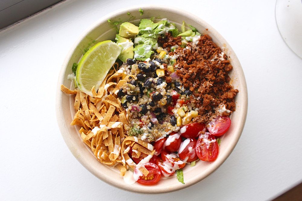Caption: A photo of a vegan salad with quinoa, seitan, black beans, corn, avocado, tomato, tortilla strips, tofu crema, and a sliced lime. (Local Guide Athena dB)