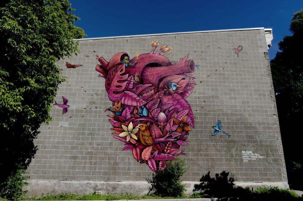 Caption: A photo of a mural created by Mexico-based artist Saner that shows a heart entagled with birds, flowers, and more. (Courtesy of MURAL Festival)
