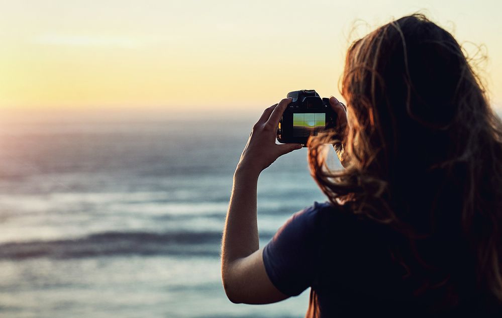 Caption: A photo of a woman taking a photograph of the ocean with a camera. (Getty Images)